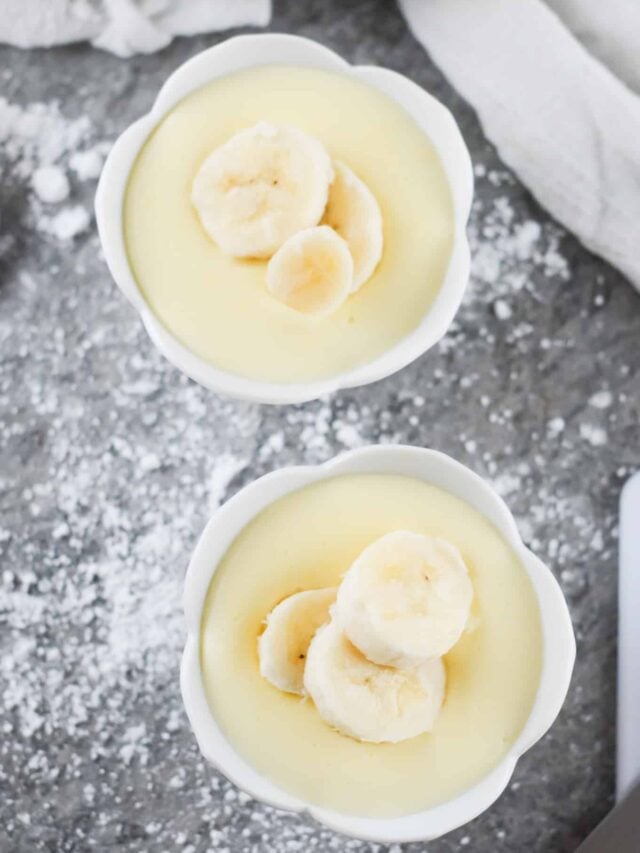 Vertical bird's-eye shot of two white bowls of banana pudding topped with three banana slices each