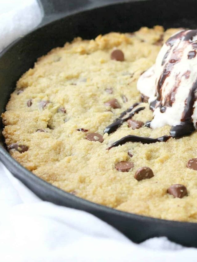 A low-carb chocolate chip skillet cookie topped with a scoop of ice cream and a drizzle of chocolate sauce.
