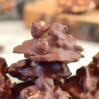 Keto chocolate peanut clusters on a plate, with blurred background emphasizing additional clusters.
