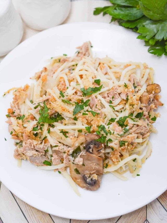 A plate of spaghetti mixed with shredded meat, mushrooms, herbs, and grated cheese resembles a classic tuna casserole but fits a keto diet. Fresh parsley and salt and pepper shakers are in the background.