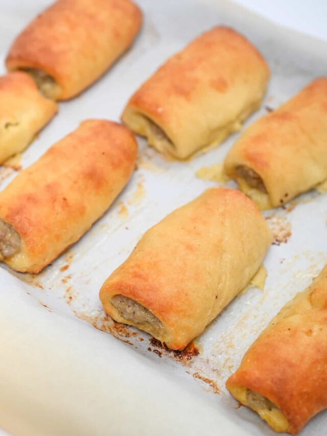 Several keto sausage rolls on a parchment-lined baking tray, slightly browned from baking.