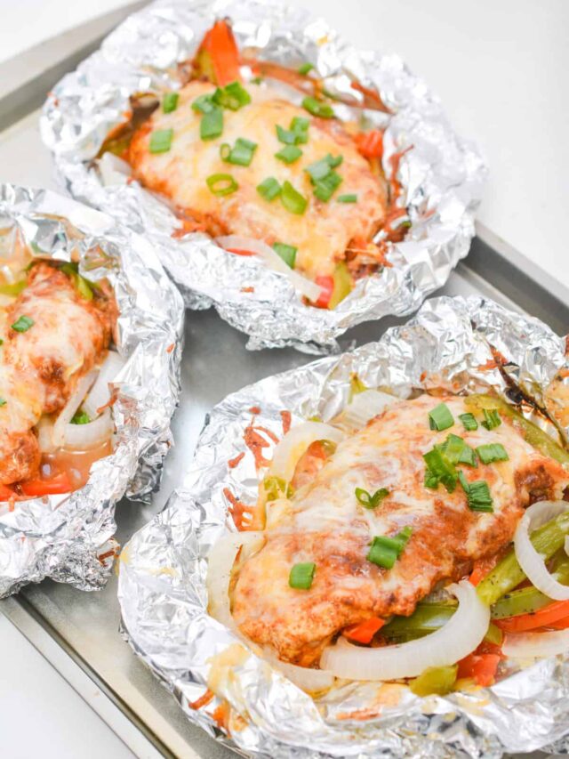 Three foil-wrapped parcels containing Tex Mex baked chicken with melted cheese, chopped green onions, and vegetables on a metal baking tray.
