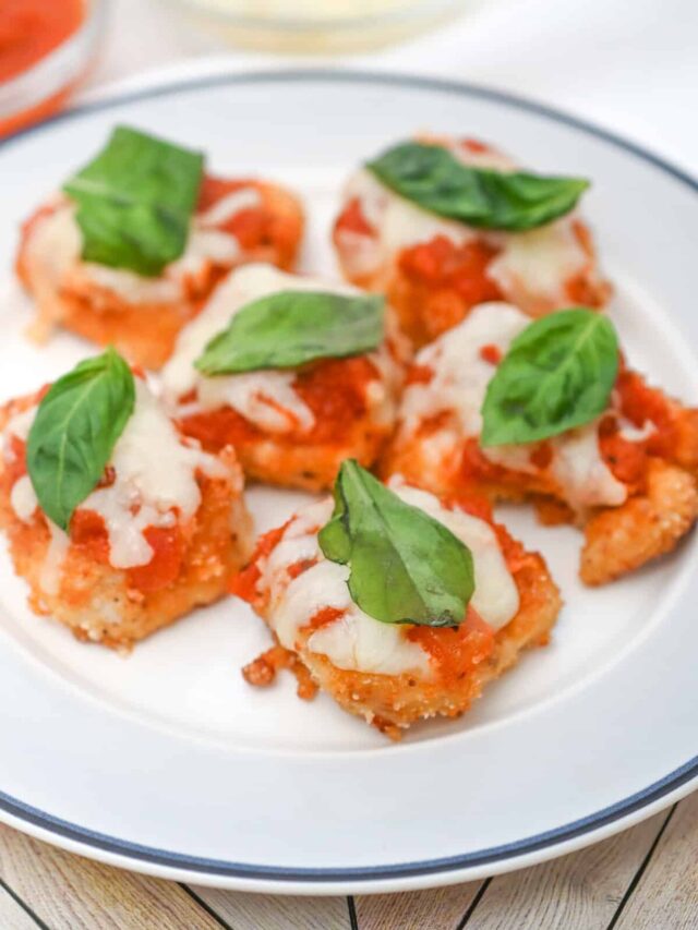 A plate of six breaded chicken bites, echoing the best low carb chicken parmesan, topped with melted cheese, tomato sauce, and fresh basil leaves.