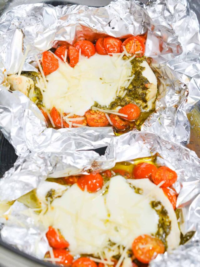 Two servings of Chicken Caprese topped with pesto, melted cheese, and cherry tomatoes, wrapped in foil and cooked to perfection. Ideal for a keto diet, this dish can be easily prepared in an air fryer for a quick and delicious meal.
