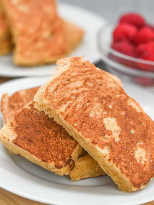 Three pieces of French toast stacked on a white plate, tempting you with their golden-brown perfection, while a bowl of raspberries adds a burst of color in the background. A delightful keto-friendly recipe for your breakfast cravings.