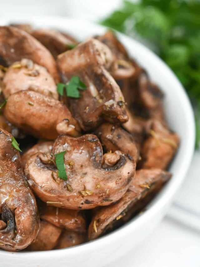 A close-up of sautéed mushrooms garnished with herbs in a white bowl.