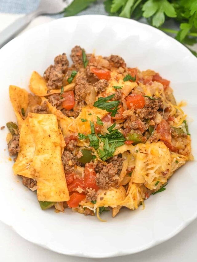 A plate of taco casserole with ground beef, tomatoes, cheese, and crispy tortilla chips garnished with parsley.
