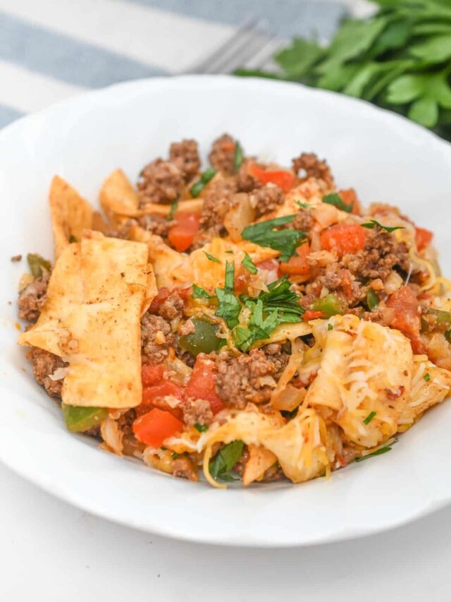 A white bowl filled with a low carb dish that includes pasta pieces, ground meat, diced tomatoes, green bell peppers, and garnished with chopped parsley.
