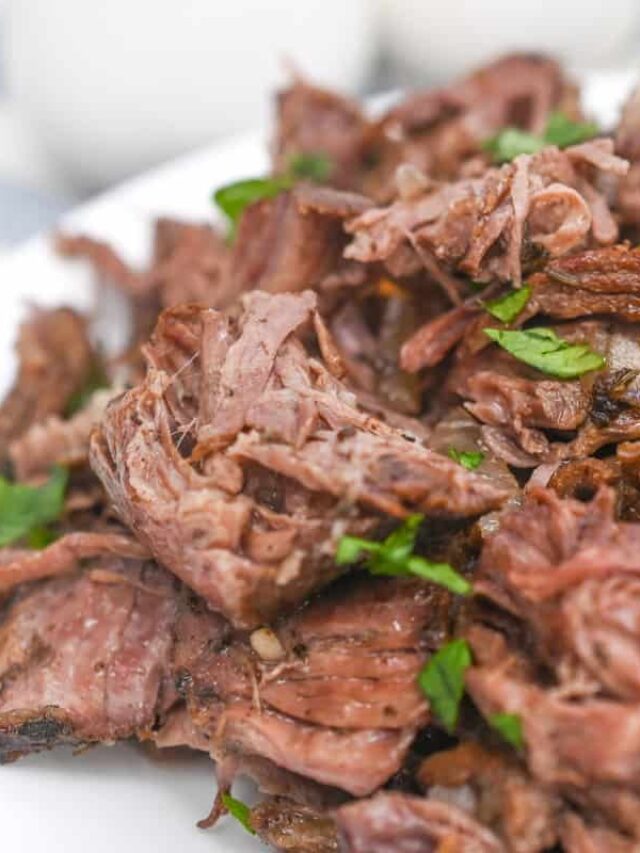 Close-up of a plate of shredded beef garnished with chopped parsley, emphasizing the texture and juiciness of the meat.