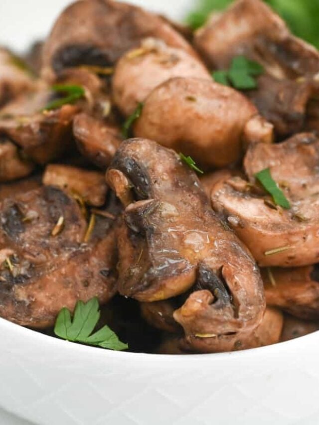 Close-up of a white bowl filled with marinated mushrooms garnished with fresh herbs. The mushrooms are cooked and seasoned to perfection, showing a slightly glossy texture—ideal for a keto-friendly dish.