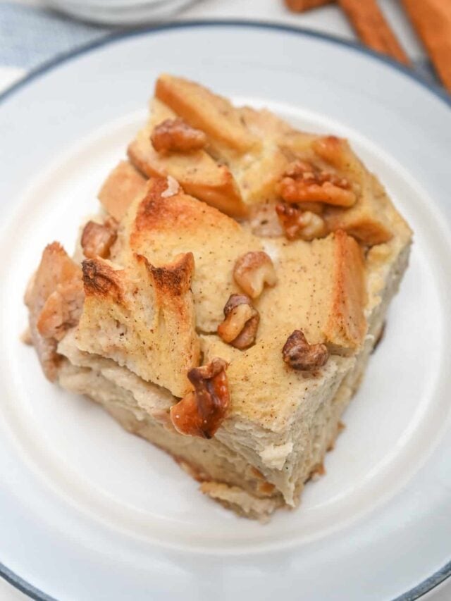 A piece of bread pudding, crafted from a low carb recipe, is elegantly topped with chopped walnuts on a pristine white plate.