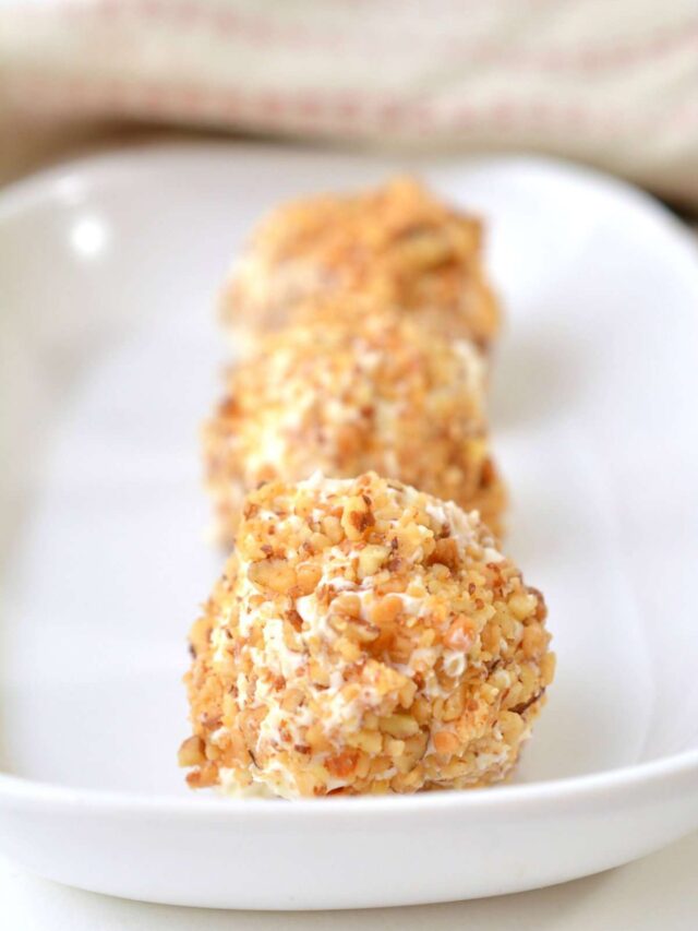 Close-up of three round, nut-coated cream cheese fat bombs arranged in a row on a white rectangular plate.