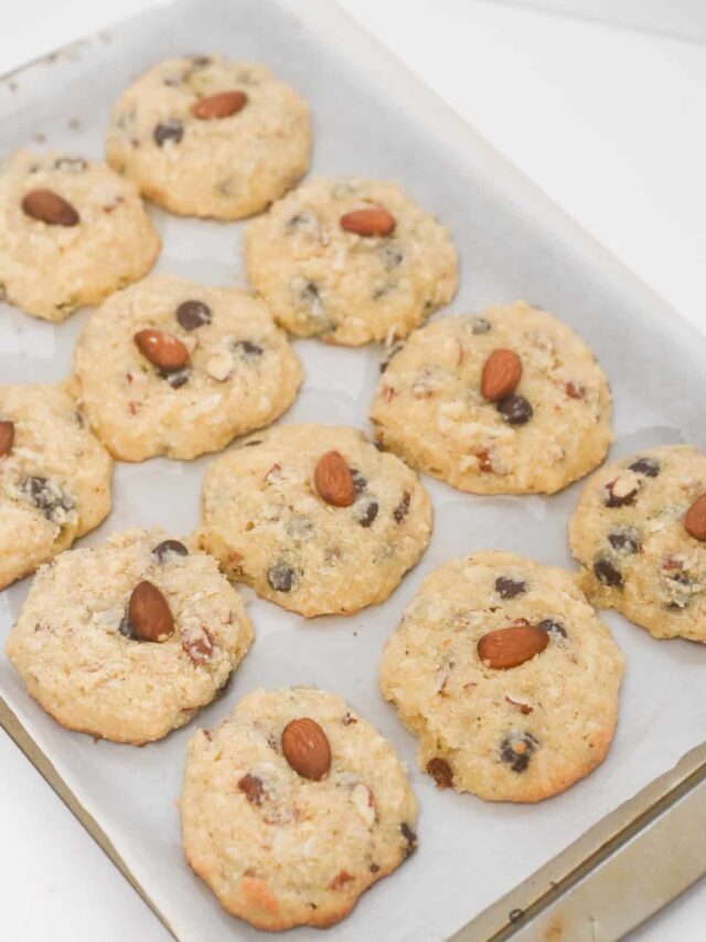 Freshly baked cookies with almonds and chocolate chips on white parchment paper.
