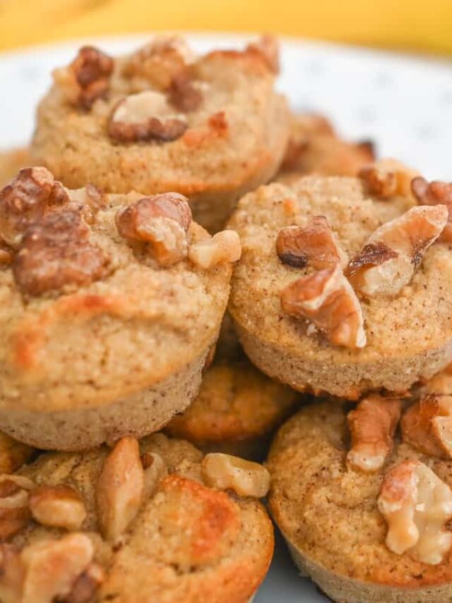A close-up of several banana nut muffins topped with chopped walnuts, arranged in a pile on a plate.