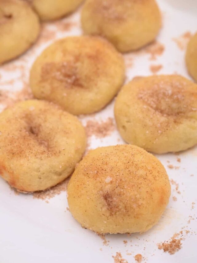 Close-up of several baked snickerdoodle cookies on a white plate, reminiscent of cinnamon rolls, all sprinkled with cinnamon and sugar.