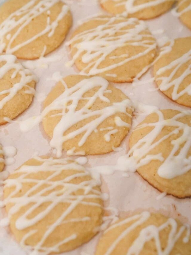 Freshly baked cookies drizzled with white icing on a pink surface.