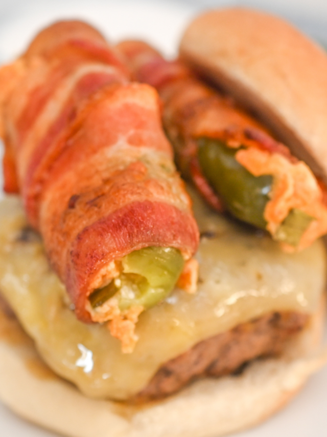 Close-up of a burger topped with a cheese, a bacon-wrapped stuffed jalapeño, and a toasted bun.