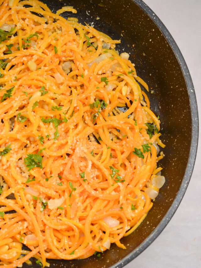 A black frying pan filled with cooked butternut squash noodles garnished with chopped parsley and grated Parmesan cheese.