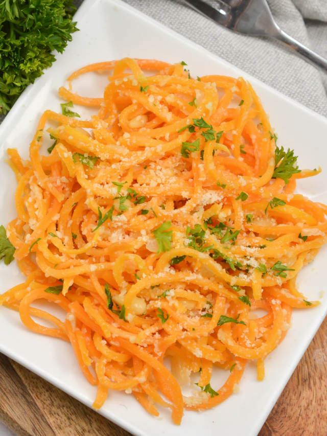 A plate of spiralized carrot noodles garnished with parsley and grated cheese, served on a white rectangular dish.