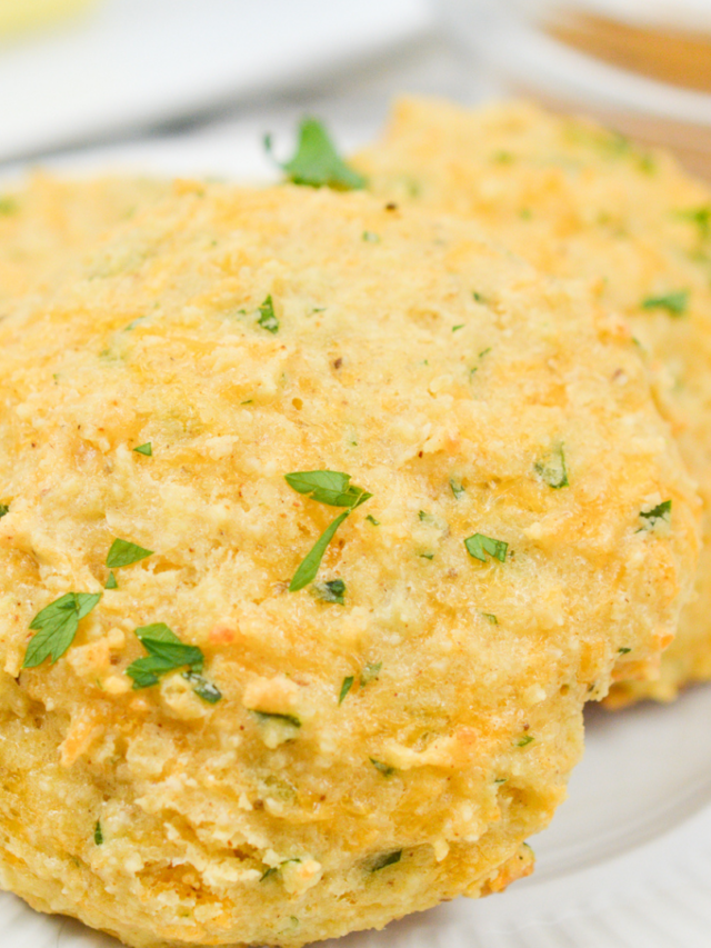 Close-up of two low-carb baked biscuits garnished with small pieces of parsley on a white plate.