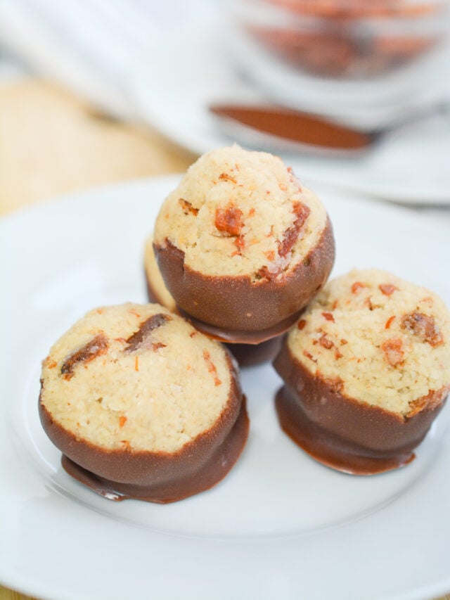 Three chocolate-covered coconut macaroons are arranged on a white plate, making for an easy low carb treat.