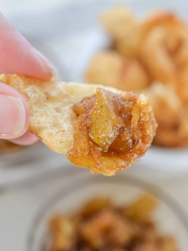 A person holds a potato chip topped with a keto-friendly apple pie salsa, with a bowl of the same mixture in the background.