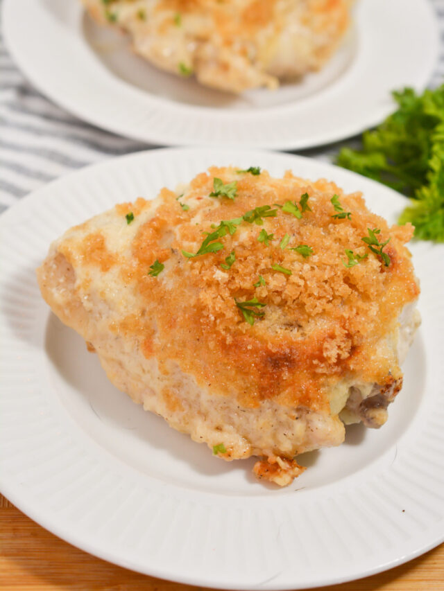 A breaded, baked chicken breast garnished with chopped parsley is served on a white plate with more parsley in the background, perfect for a keto-friendly meal.