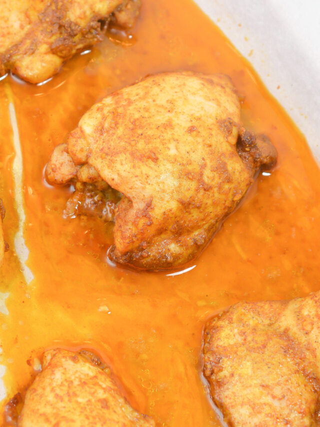 Baked chicken thighs with a golden brown crust sit in a pan with orange-colored juices, making this keto-friendly recipe irresistible.