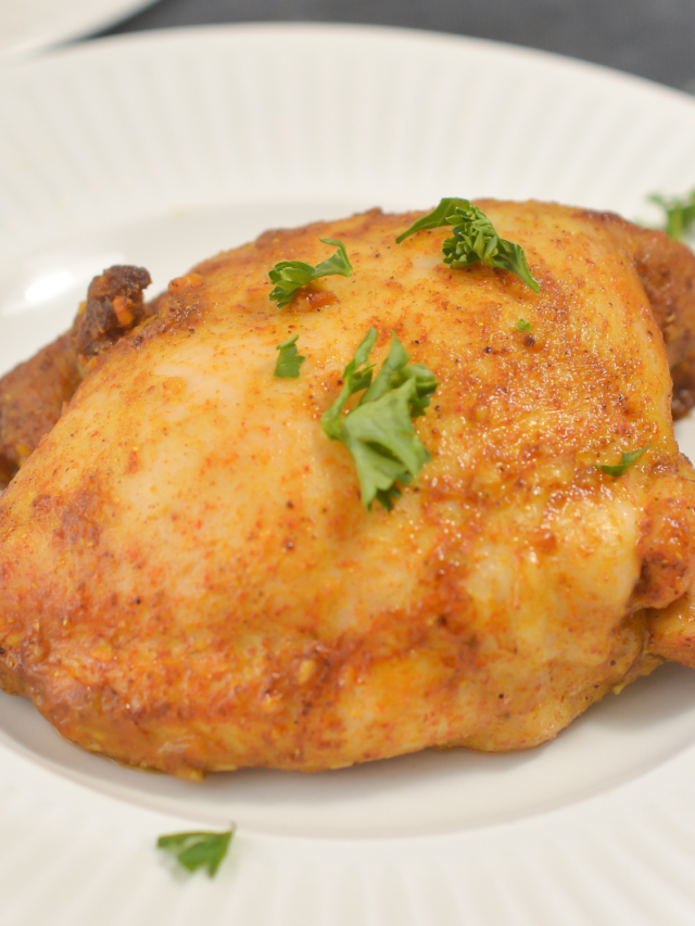 A cooked chicken thigh seasoned with herbs and spices is served on a white plate, garnished with small sprigs of parsley, making it a perfect addition to your keto recipe collection.